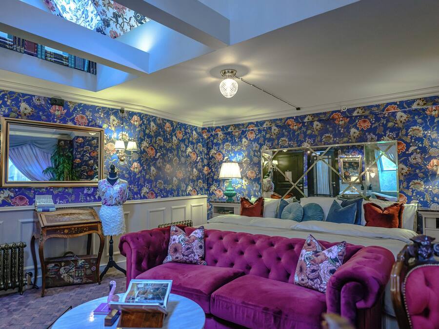 A room with a floral wallpaper, a large mirror, a tufted sofa, and a ceiling fan.
