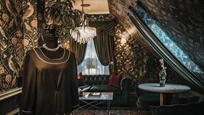A room with a mannequin dressed in a black outfit, a chandelier, a green sofa, and patterned wallpaper. - Charmante Skostredet Hôtel (Bergen)