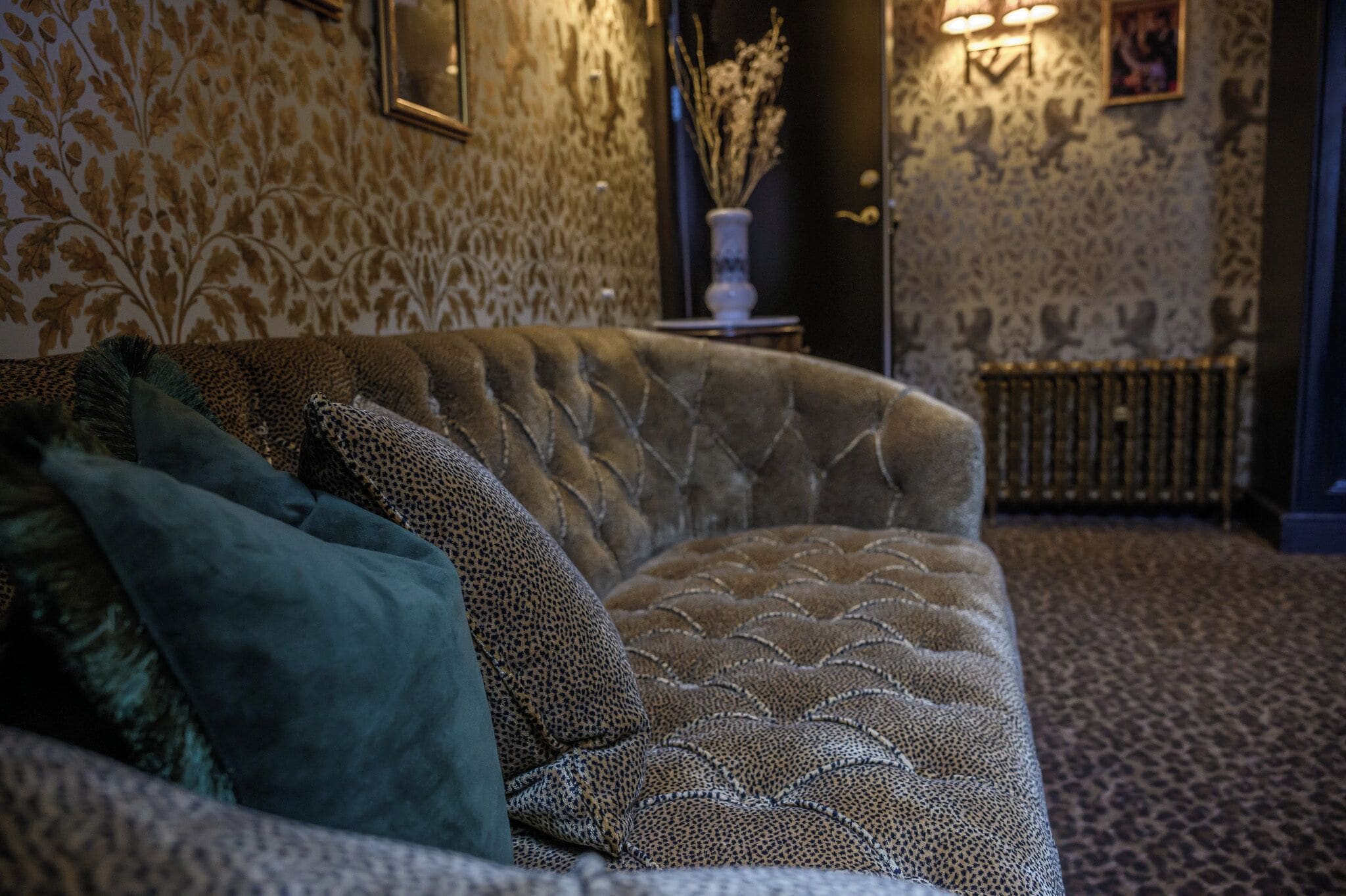 A plush sofa with a patterned fabric, a decorative vase with dried plants, and a patterned carpet.