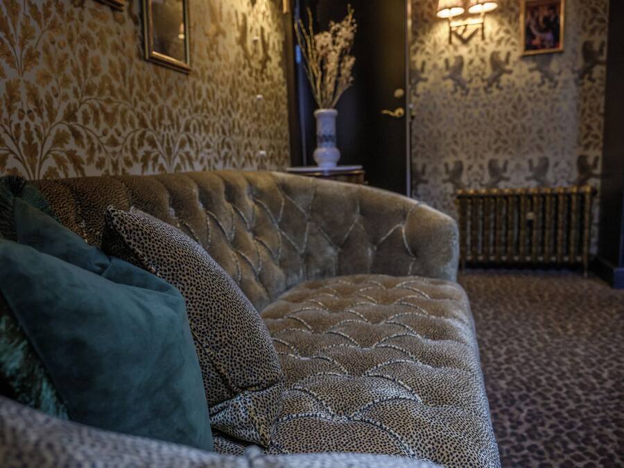 A plush sofa with a patterned fabric, a decorative vase with dried plants, and a patterned carpet.