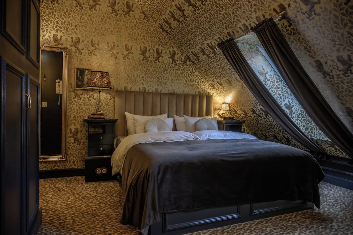 Ein Schlafzimmer mit einem großen Bett, einem Nachttisch, einer Lampe und einem Spiegel.