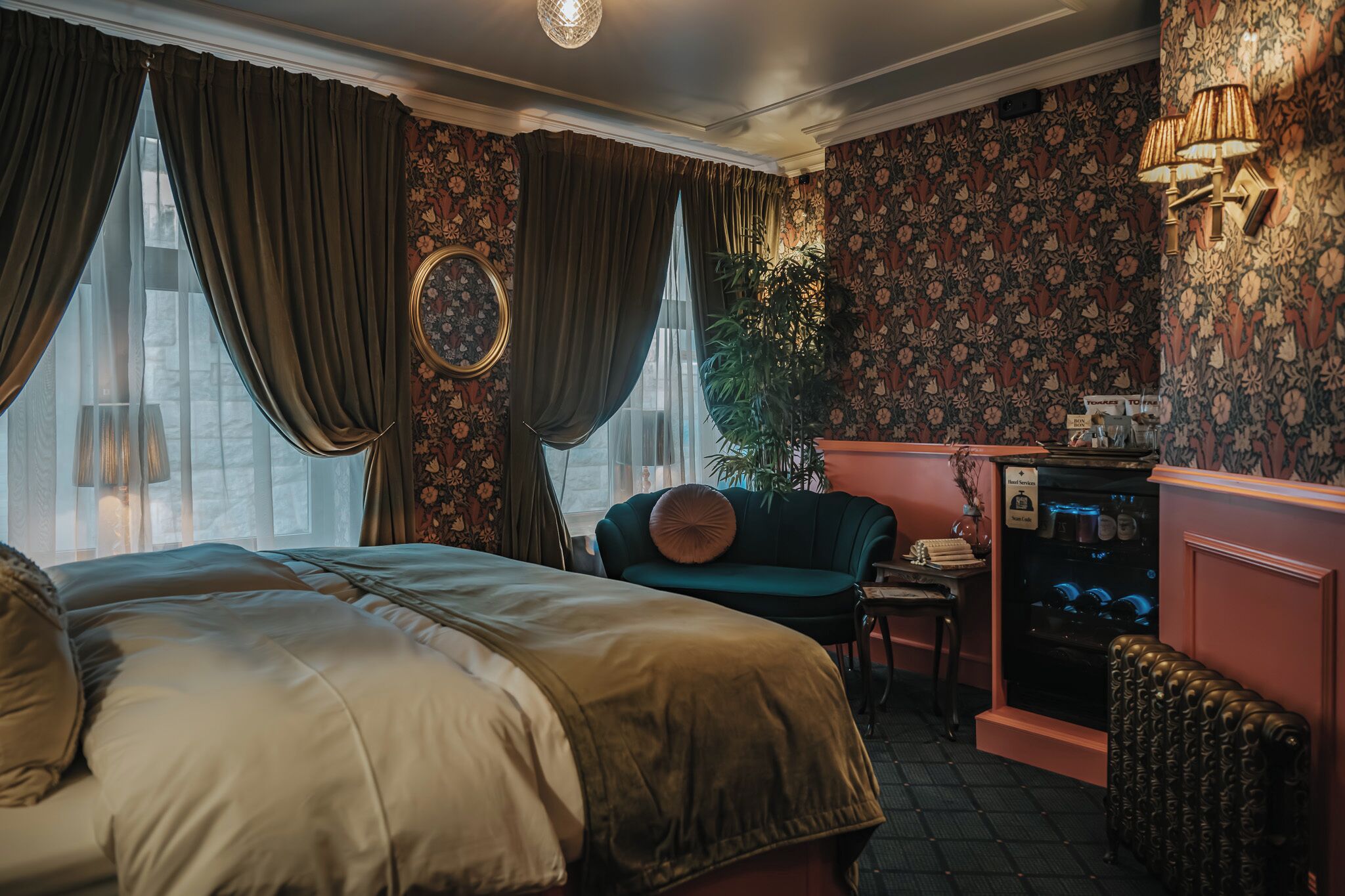 A bedroom with a large bed, a green armchair, a small table, a radiator, and a wall-mounted shelf with items.
