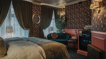 Un dormitorio con una cama grande, un sillón verde, una mesita, un radiador y un estante en la pared con objetos.