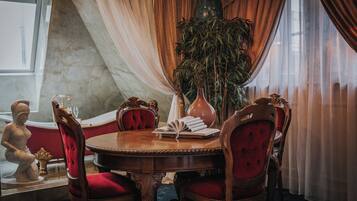 A dining area with a round wooden table, red upholstered chairs, a vase, and a potted plant.