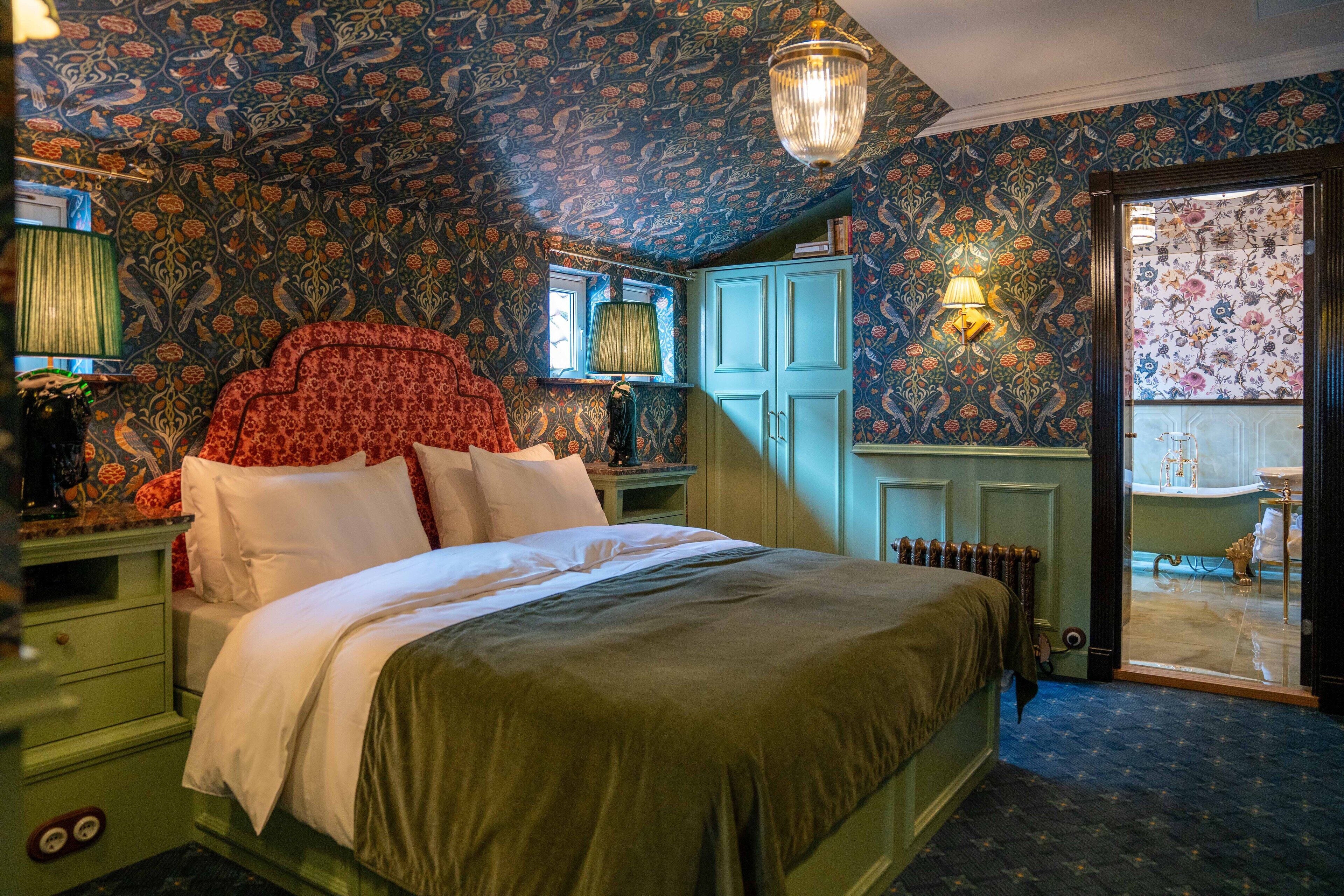 Un dormitorio con una cama grande, mesitas de noche verdes, un aparador y un baño visible a través de una puerta abierta.