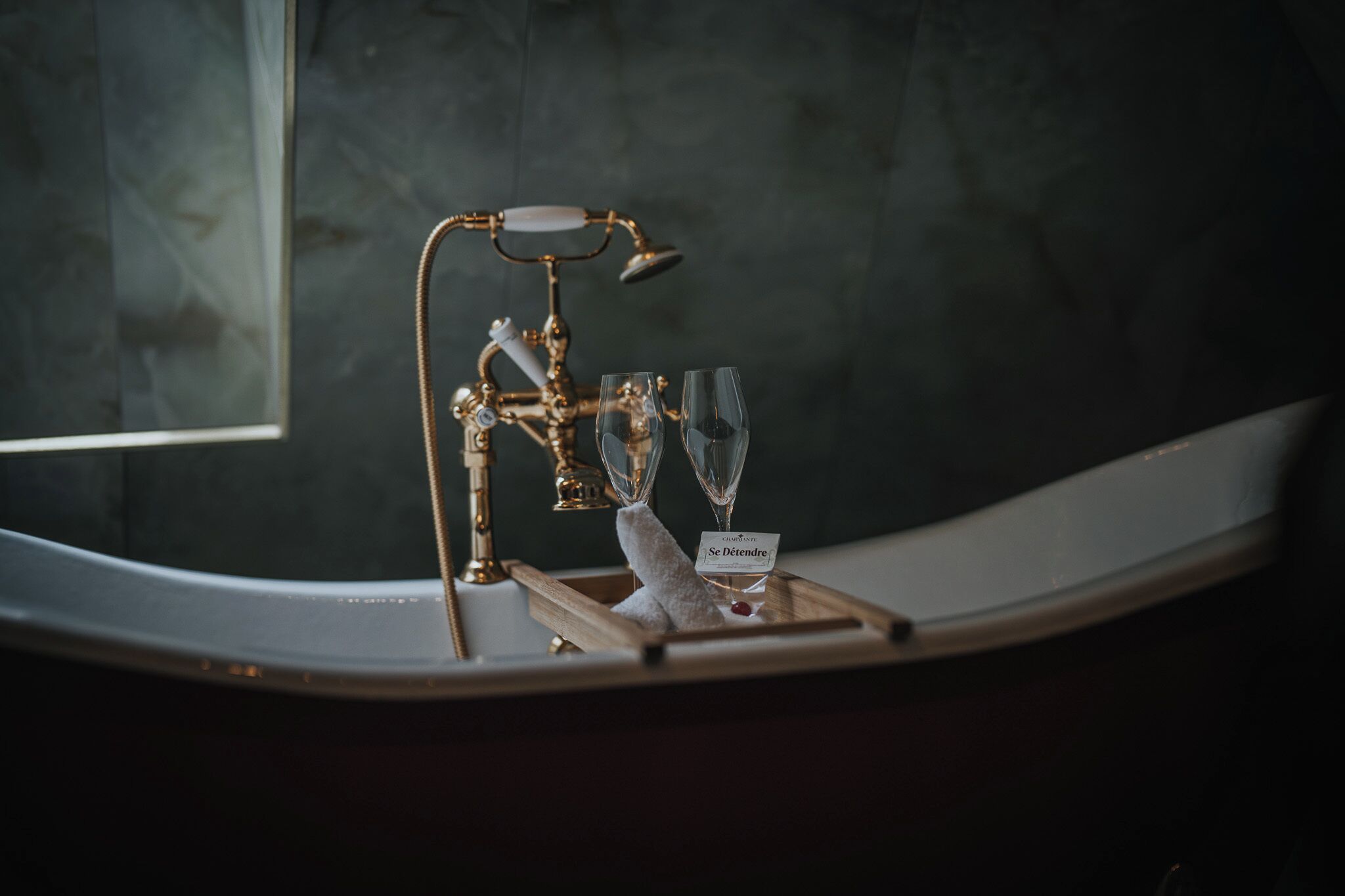 A bathroom vanity with a gold faucet, two wine glasses, and a tray with a name tag.
