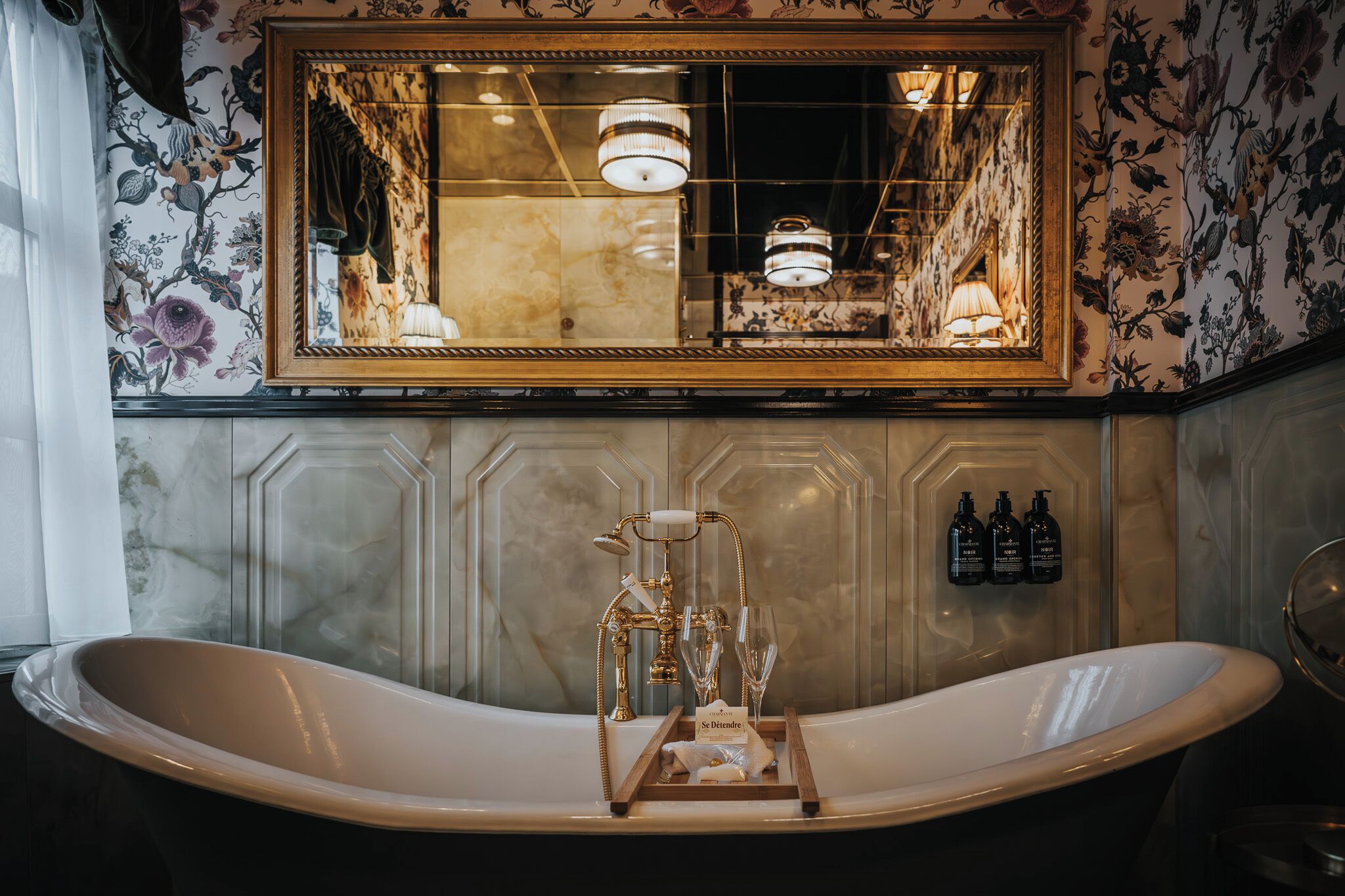 A bathroom with a freestanding bathtub, a large mirror, and a chandelier.