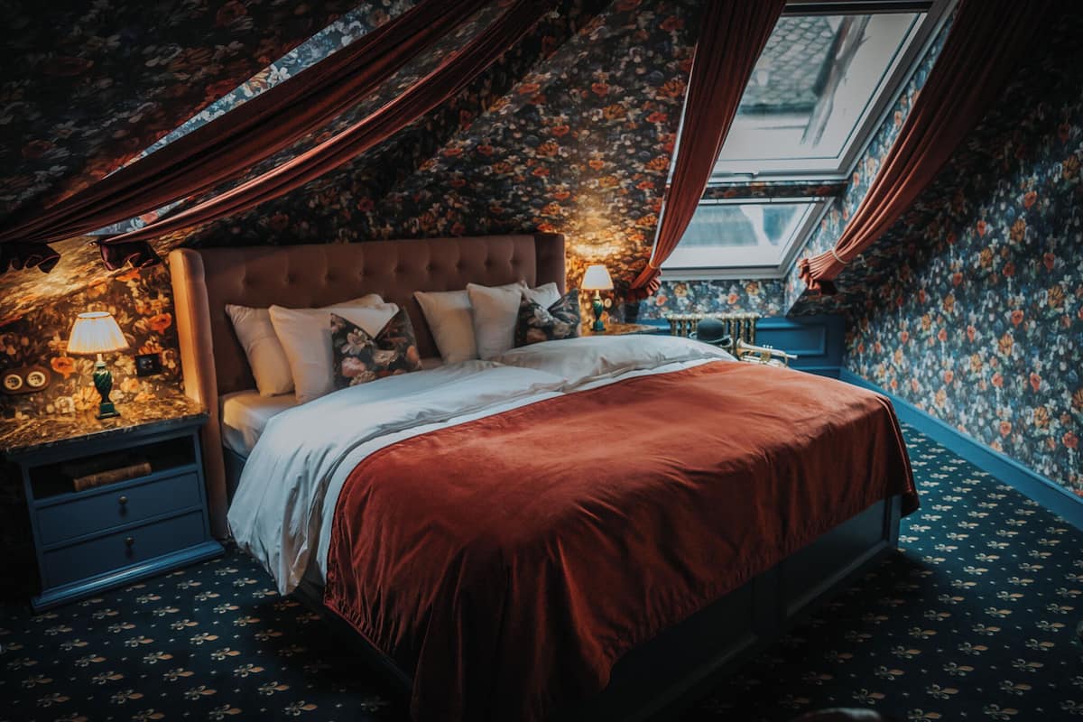 Ein Schlafzimmer mit einem großen Bett, floralem Wandpapier und einem Dachfenster.