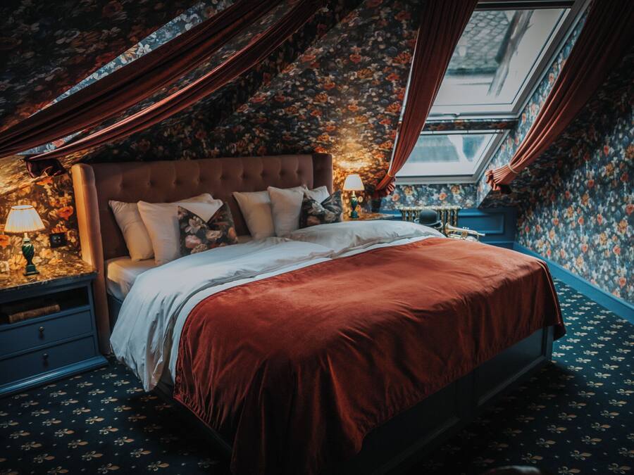 Un dormitorio con una cama grande, papel tapiz floral y un tragaluz.