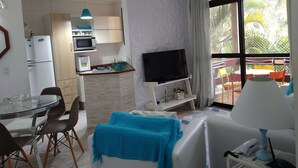 Un espacio habitable compacto con kitchenette, comedor, zona de estar con televisor y balcón con mobiliario exterior.