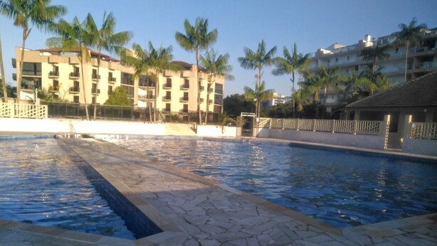 Una piscina con baldosas de piedra, rodeada de palmeras y un edificio con varios balcones.