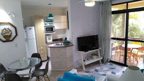 Un espacio habitable compacto con comedor, kitchenette, televisión y un balcón con mobiliario exterior.