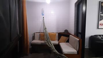 A room with a ceiling fan, a hammock, a sofa with cushions, and a poster on the wall.