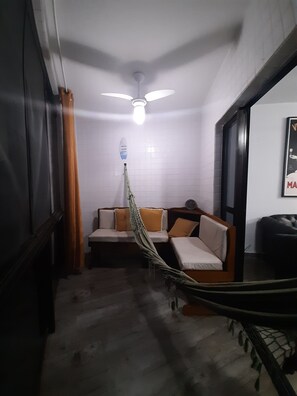 A room with a ceiling fan, a hammock, a sofa with cushions, and a poster on the wall.