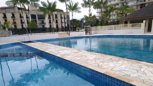 Una piscina con azulejos azules, rodeada por un solado de baldosas y palmeras.