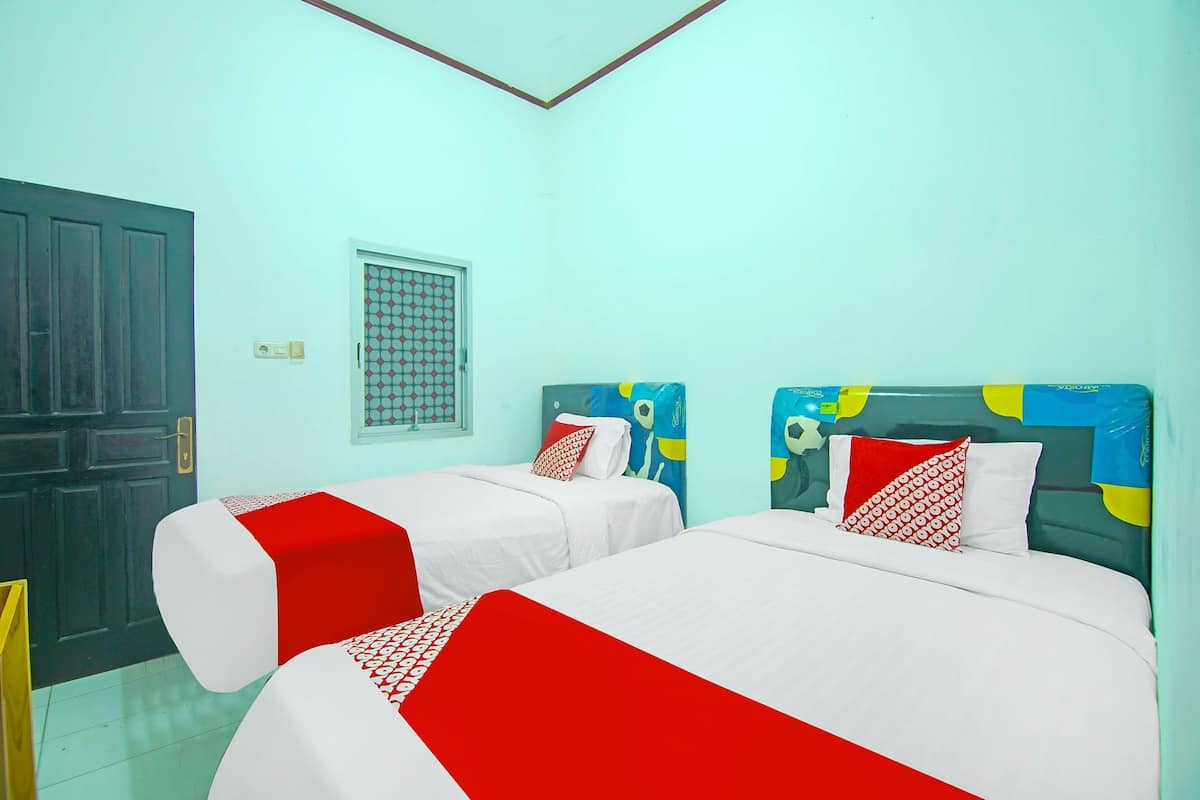 Een kamer met twee bedden, elk voorzien van witte beddengoed en rode accenten, een donkerhouten deur en een raam met een versierd rooster.