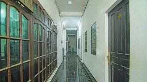 Un couloir doté d’un sol carrelé, de portes en bois et de grandes fenêtres sur le côté gauche.