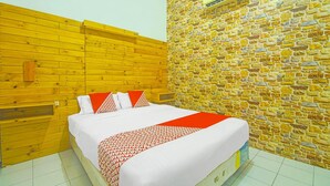 Une chambre avec une tête de lit en bois, un mur en pierre, un lit recouvert d’une literie blanche et d’un couvre-lit à motifs rouges et blancs, ainsi qu’un petit meuble en bois.