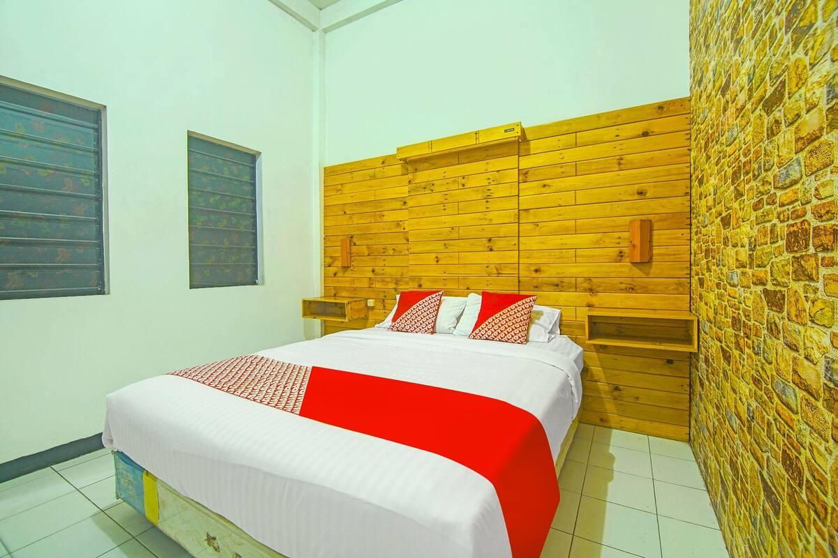 Een hotelkamer met een houten hoofdeinde, een bed met rood-witte beddengoed en een muur met een steenmotief.