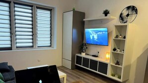 A living room with a TV, a laptop, and a remote control on a wooden table.