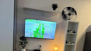 A modern living room with a flat-screen TV mounted on a white wall, a white entertainment unit below, a small potted plant, and a round floor lamp.