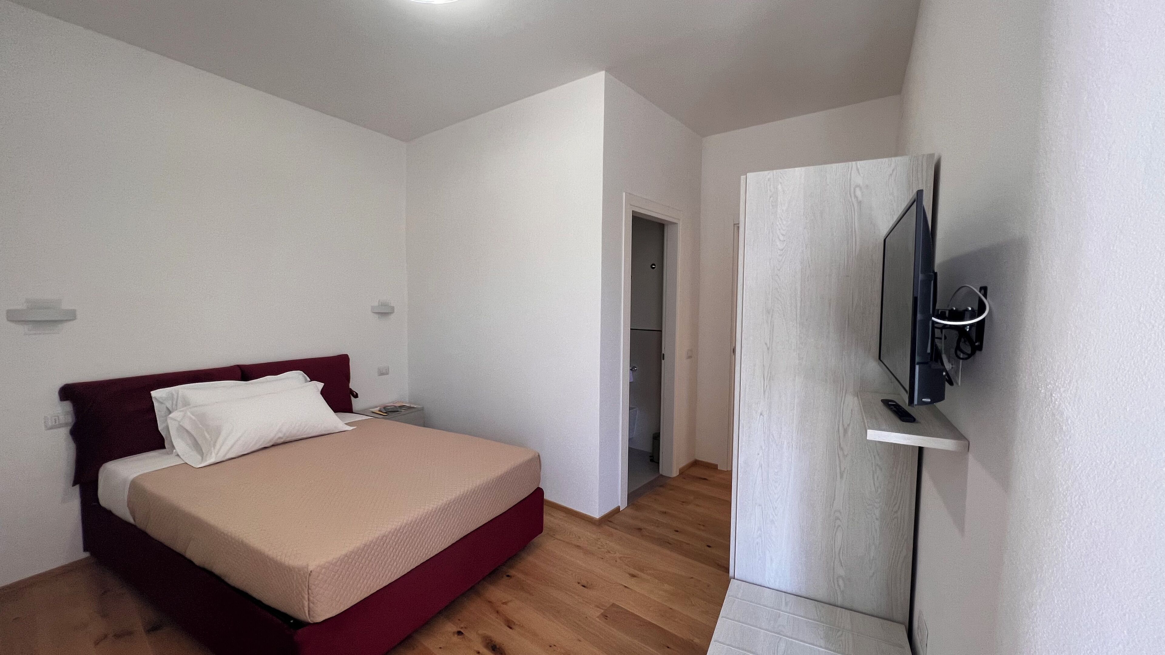 Une chambre à coucher avec un lit, un téléviseur fixé au mur et une porte donnant sur une autre pièce.