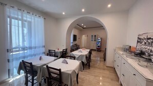 A dining area with tables and chairs, a kitchen area with cabinets, and a view through an archway. - B&B Aurora (San Marcello Piteglio)