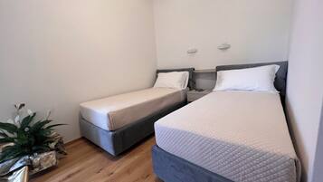 A small, clean room with two single beds, a bedside table with a lamp, and a potted plant.