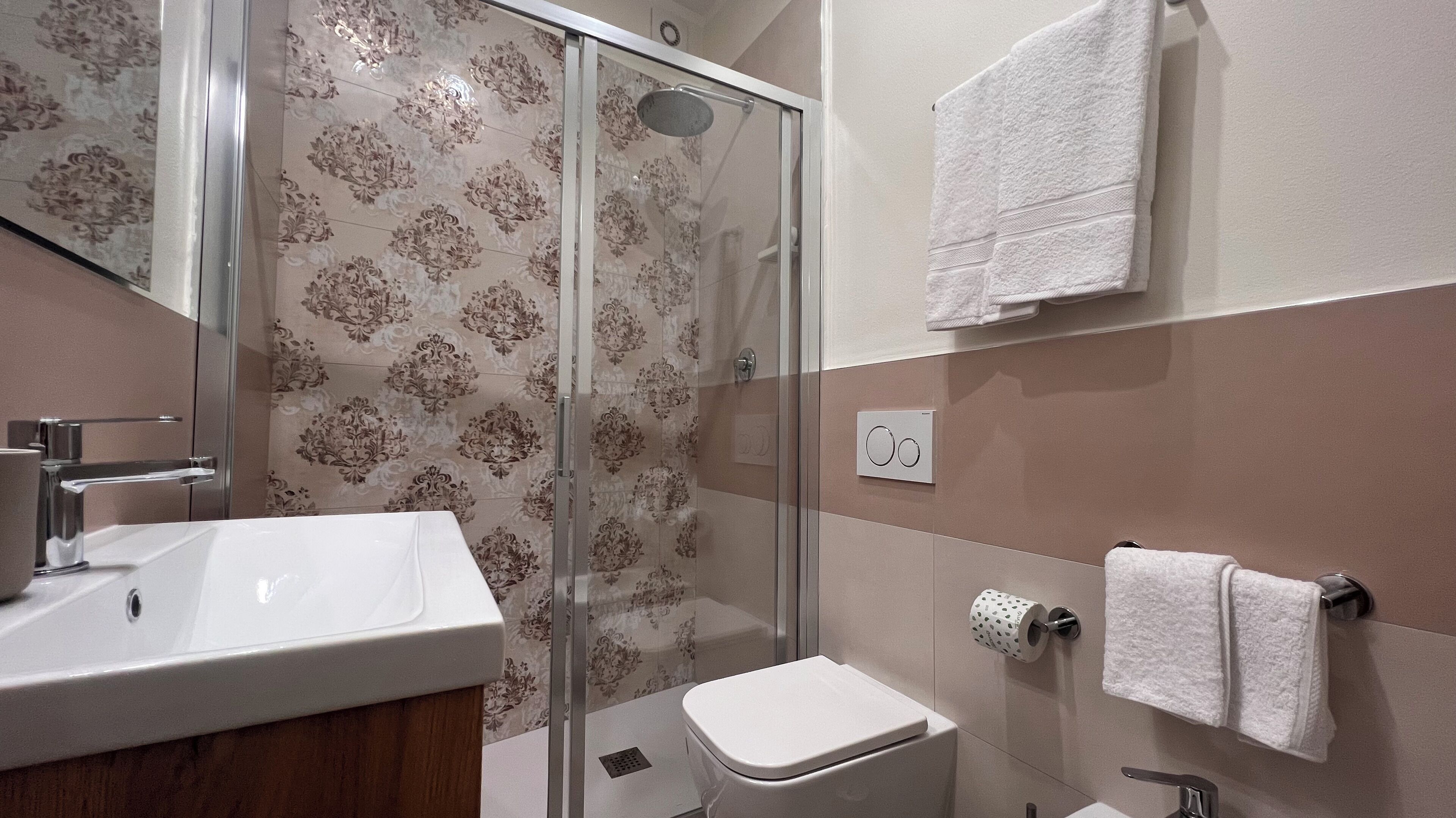 A bathroom with a glass shower enclosure, a sink, a toilet, and a towel rack.