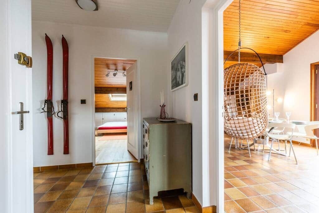 A room with a wooden ceiling, a dining area with a hanging chair, and a view into another room with a bed.