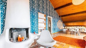 Een modern interieur met een open haard, een witte stoel, een getextureerd vloerkleed en een eethoek met tafels en stoelen.