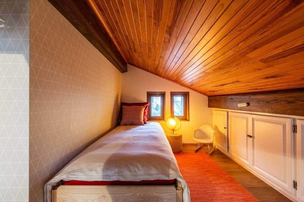 Ein Schlafzimmer mit Holzboden, einem Bett, einem Nachttisch mit Lampe, einem Sessel und einem Kleiderschrank.