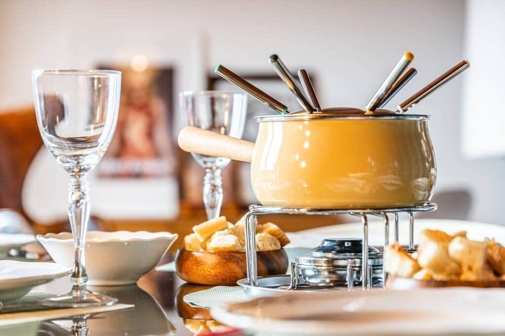 A dining table with a fondue pot, a glass, and a bowl of bread.