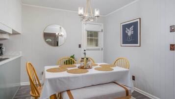 A dining area with a white table, wooden chairs, a chandelier, and a framed artwork on the wall.