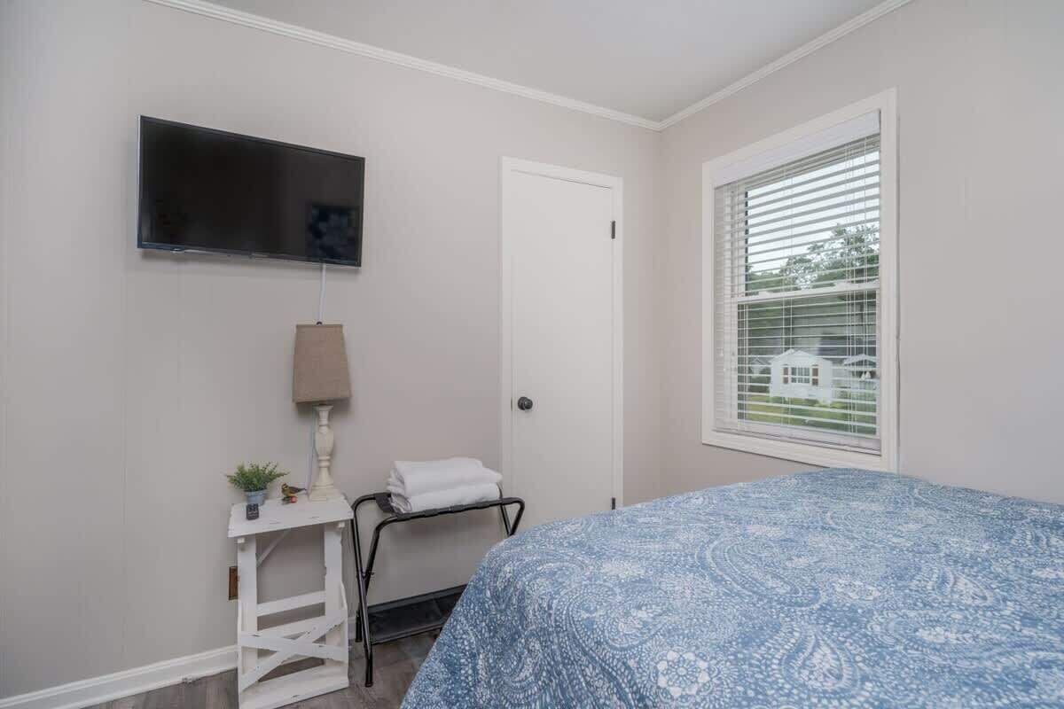 A bedroom with a bed, a TV mounted on the wall, a bedside table with a lamp, and a window with blinds.