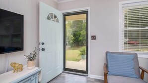 A room with a sliding glass door leading to a backyard, a television mounted on the wall, and a chair with a cushion.