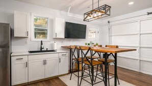 A modern kitchen with white cabinetry, a wooden dining table, and a black TV mounted above the counter.