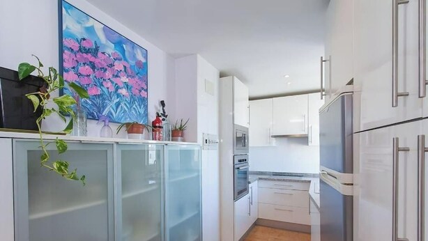 Una cocina moderna con armarios blancos, un refrigerador de acero inoxidable y un cuadro de flores en la pared.