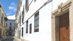 Una calle estrecha con un edificio blanco, una puerta de madera y una línea amarilla que delimita la acera.