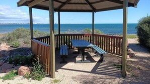 Un área de picnic techada con una mesa y bancos, con vista al mar.