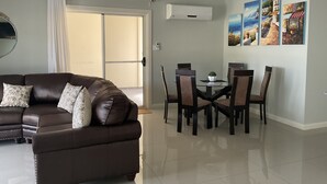 Una sala de estar moderna con un sofá de cuero marrón, una mesa de comedor con sillas y un ventilador de techo.