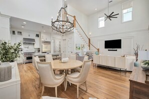 A spacious kitchen with white cabinetry, a dining area with a round table and chairs, a staircase, and a mounted flat-screen TV. - Watercolor Resort |Private Pool | 6 Pass Golf Cart (Santa Rosa Beach)