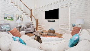 Ein geräumiges Wohnzimmer mit Treppe, einem Wand-Fernseher und einer gemütlichen Sitzecke mit Couchtisch.