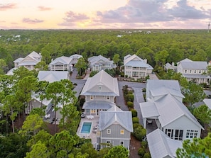 A residential area with multiple houses, a swimming pool, and a forested background. - Watercolor Resort |Private Pool | 6 Pass Golf Cart (Santa Rosa Beach)