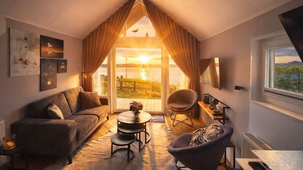 A cozy room with a sloped ceiling, a sofa, a chair, a small table, and a view of the outdoors. - Tiny House Holland by the lake. A quiet, comfortable break on the beach by the water. (Lathum)