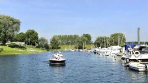 A marina with boats docked and a small boat with people on it. - Tiny House Holland by the lake. A quiet, comfortable break on the beach by the water. (Lathum)