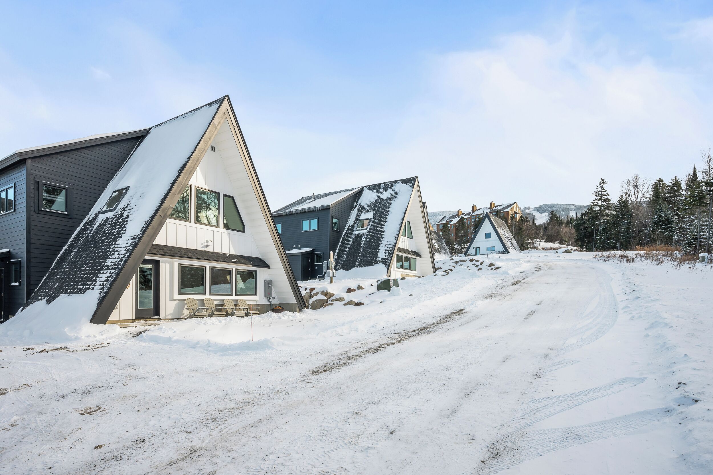 Una hilera de casas modernas de forma triangular con tejados cubiertos de nieve y un cielo despejado.