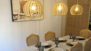 A dining area with a long table set for six, featuring white tablecloths, gold-rimmed plates, and wicker chairs. - Cosy, spacious air-conditioned apartment with all mod cons (Puget-ville)