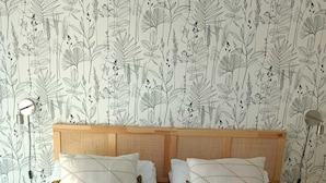 A bedroom with a bed, two bedside tables, and a wall with a botanical wallpaper pattern. - Cosy, spacious air-conditioned apartment with all mod cons (Puget-ville)