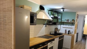 A modern kitchen with a stainless steel refrigerator, a microwave, a built-in oven, and a sink with a wooden countertop. There are cabinets with black handles and a backsplash with white tiles. - Cosy, spacious air-conditioned apartment with all mod cons (Puget-ville)